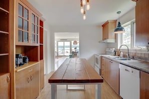 Una cocina con armarios de madera, una mesa de madera, un lavavajillas y un ventanal.
