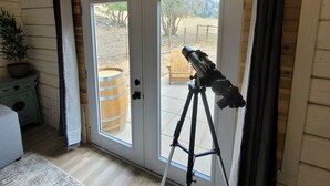A room with a telescope on a tripod near a sliding glass door leading to an outdoor area.