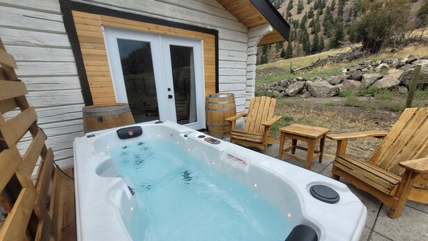 A hot tub outside a cabin with wooden chairs and a wooden deck.