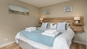 A neatly made bed with a blue throw blanket, white pillows, and a wooden headboard.