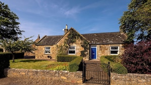 A stone house with a blue door, a stone wall in front, and a gravel driveway.