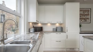 A modern kitchen with white cabinets, a stainless steel sink, and a built-in oven.