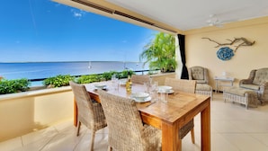A dining area with a view of the sea, wicker furniture, and a ceiling fan.