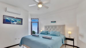 A bedroom with a bed, a ceiling fan, a nightstand, a lamp, and a window with a view.