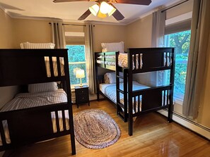 A room with bunk beds, a small desk with a lamp, a window with curtains, and a ceiling fan. - Spacious ski chalet with pool table & mountain views (Rutland)
