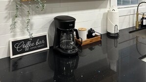Una cocina con dos estantes de madera, una cafetera y un letrero que dice 'Coffee bar open daily'.