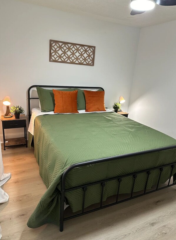 A neatly arranged bedroom with a green bedspread, two nightstands, and a decorative wall piece.