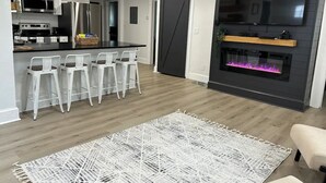 Cocina moderna con armarios blancos, electrodomésticos de acero inoxidable y una puerta corrediza negra que da a un comedor con sillas blancas.