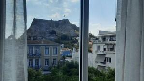 Blick aus einem Fenster mit Vorhängen auf ein Gebäude, im Hintergrund ein felsiger Hügel.