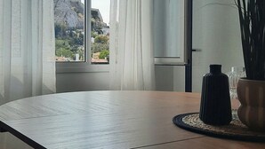Ein geräumiges Zimmer mit großem Tisch, einer Bank und Blick auf eine gebirgige Landschaft durch transparente Vorhänge.