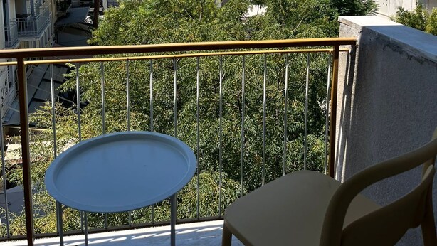 Ein Balkon mit Tisch und Stuhl, mit Blick auf eine Stadtlandschaft, einschließlich Gebäude und eines markanten Felsenhügels im Hintergrund.