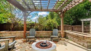 A covered outdoor patio with a fire pit, two Adirondack chairs, and a pergola structure.