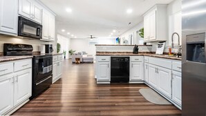 A modern kitchen with white cabinets, stainless steel appliances, and a wooden floor.