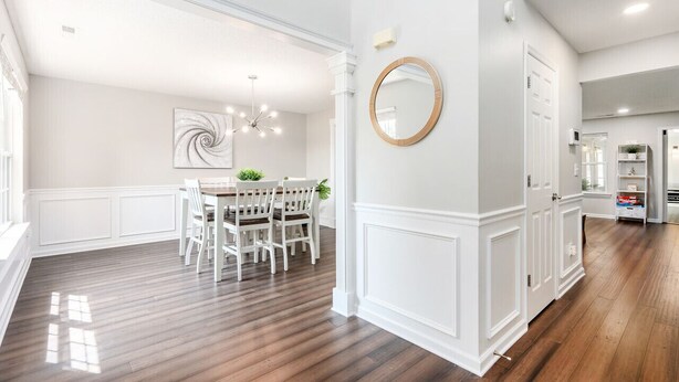A spacious dining area with a white table and chairs, a large mirror, and a modern chandelier.