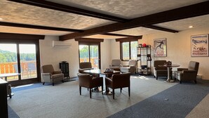 A spacious indoor area with a high ceiling, large windows, and a view of a balcony. There are several chairs and a table with a chess set. - Charming, ski-in, ski-out, lake-view chalet w/ 10 bedrooms, kitchen and AC. (Upson)