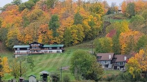 A lakeside property with a large house and smaller buildings, surrounded by autumn foliage. - Charming, ski-in, ski-out, lake-view chalet w/ 10 bedrooms, kitchen and AC. (Upson)