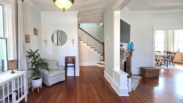 A spacious living room with hardwood floors, a staircase, a fireplace, and a large mirror.