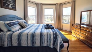 A bedroom with a bed, a dresser, a mirror, and a painting on the wall.