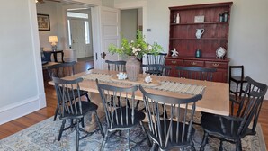A dining area with a wooden table, black chairs, a woven placemat, a vase with flowers, and a wooden cabinet with decorative items.