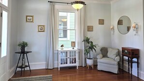 A room with a wooden floor, a white cabinet, a white sofa, a potted plant, a small table with a lamp, a ceiling fan, and a large mirror on the wall.