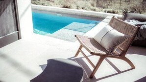 A lounge area with a wicker chair and a cushion, overlooking a swimming pool. - Terra Segreda (Volos)