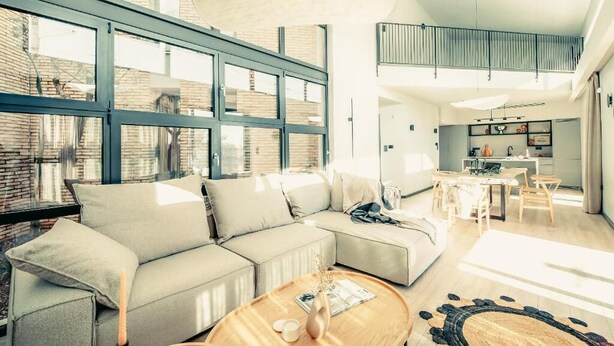 A spacious living area with a large sectional sofa, a round coffee table, and a dining area with a kitchen in the background. - Terra Segreda (Volos)