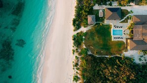 An aerial view of a beachside resort with a swimming pool, multiple buildings, and lush greenery. - YellowBird Estate in Double Bay - Fully Staffed! (North Palmetto Point)