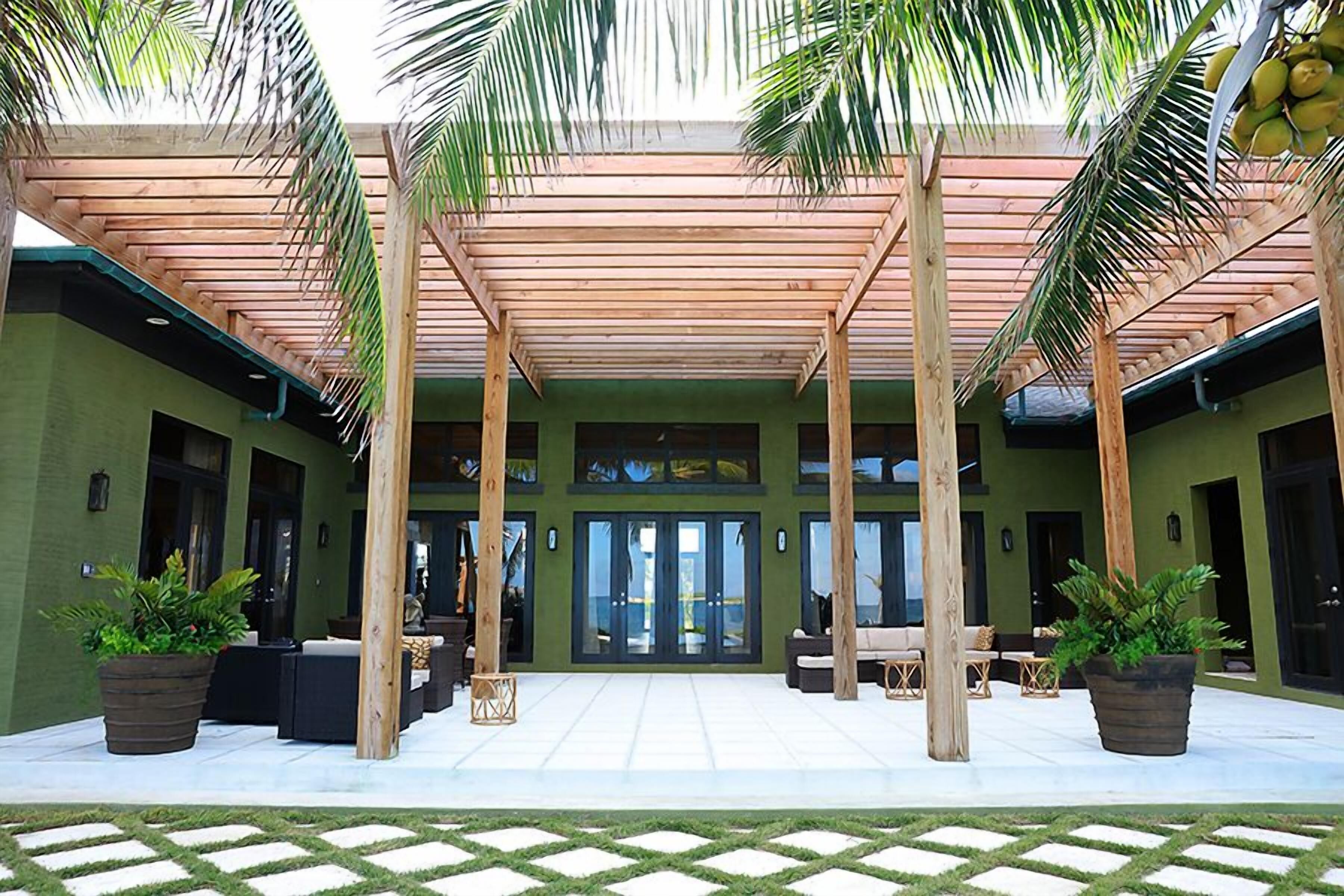 Un espacio al aire libre techado, con vigas de madera, plantas en macetas y arreglos de asientos.
