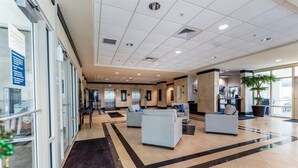 A spacious lobby with a reception desk, seating area, and a large window providing a view of the outdoors. - Crystal Tower Corner w/ 2 Balconies, 3 Pools, Lazy River, Free Daily Activities (Gulf Shores)