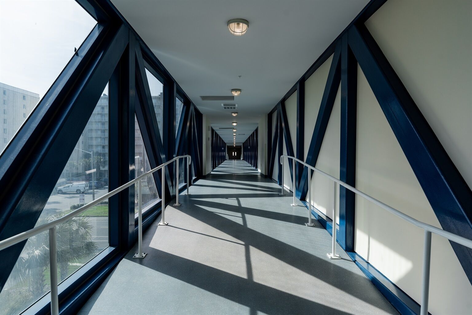Un couloir doté de grandes fenêtres et de rampes en métal, qui mène à une sortie située au loin.