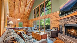 A cozy log cabin interior with a fireplace, large windows, and a comfortable seating area. - Spring With A View! Hot Tub, Theater, Pool Table (Gatlinburg)