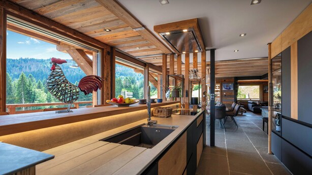 A modern kitchen with wooden beams, a large window with a view of a forest, and a unique rooster sculpture. - Chalet K1027 - mountain stay 14p spa and Mont Blanc views - OVO Network (Cordon)