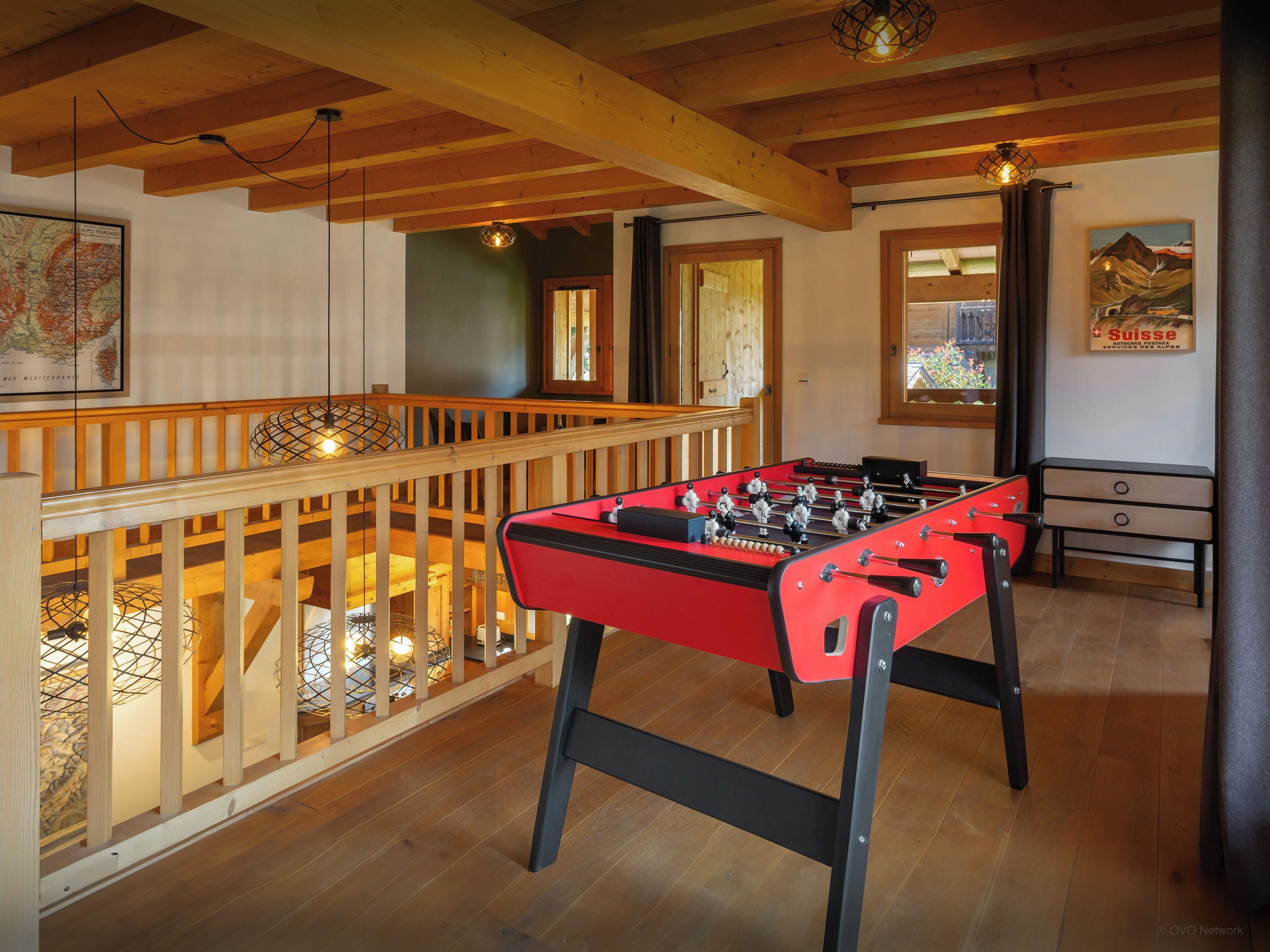 A cozy room with a foosball table, wooden beams, and a balcony with a railing.