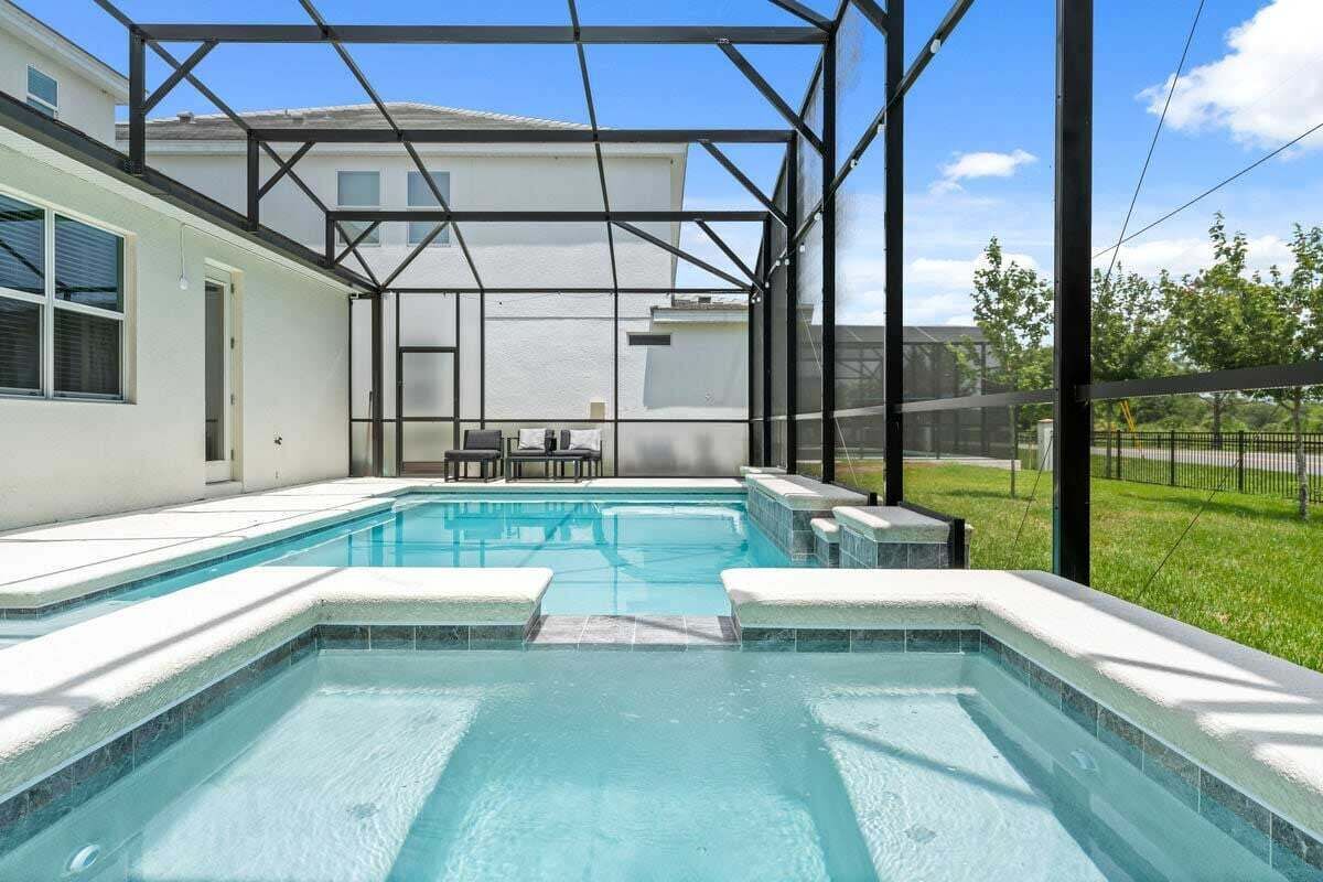 A rectangular swimming pool with a glass enclosure, surrounded by a white wall and a grassy yard.