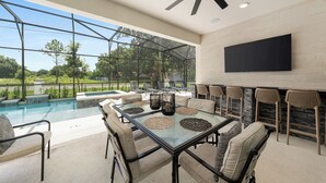 A spacious outdoor patio with a glass-top table, cushioned chairs, and a ceiling fan.