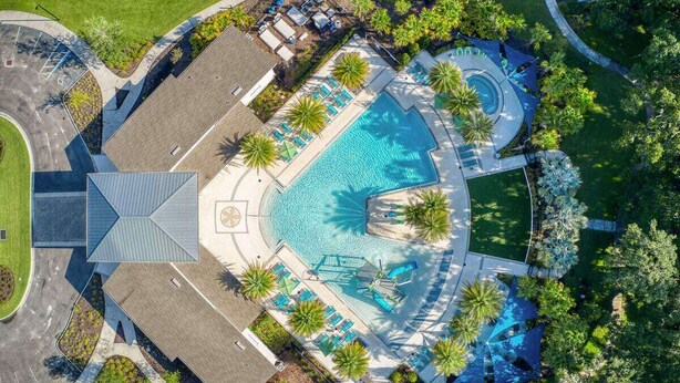 An aerial view of a resort with a central swimming pool, lounge areas, and palm trees.