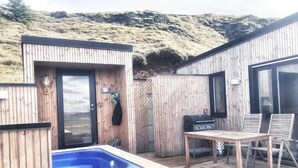 A wooden deck with a hot tub, a grill, and a table with chairs. - Modern mountain-view cottage in Golden Circle with outdoor Hot Tub & Sauna (Hrunamannahreppur)