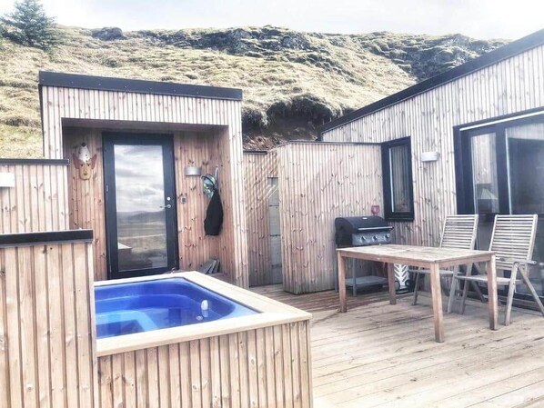 A wooden deck with a hot tub, a grill, and a table with chairs.