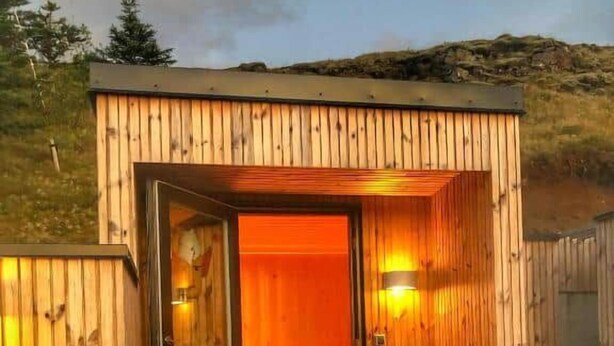 A wooden cabin with a glass door leading to an interior with a warm light source. - Modern mountain-view cottage in Golden Circle with outdoor Hot Tub & Sauna (Hrunamannahreppur)