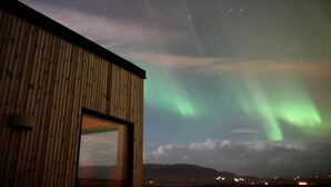 A building with a wooden exterior and a large window. - Modern mountain-view cottage in Golden Circle with outdoor Hot Tub & Sauna (Hrunamannahreppur)