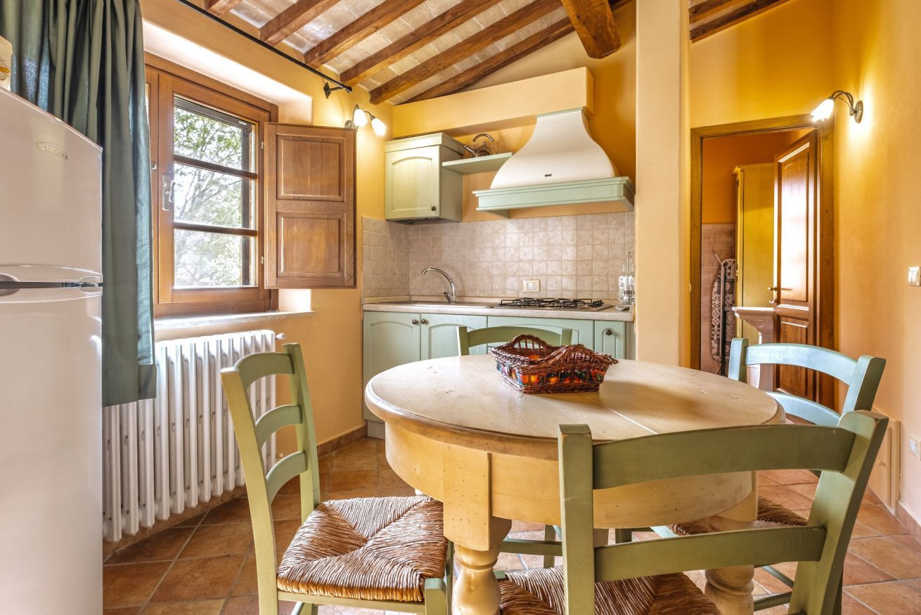 Una cocina con una mesa redonda, sillas, una ventana, armarios y un radiador.