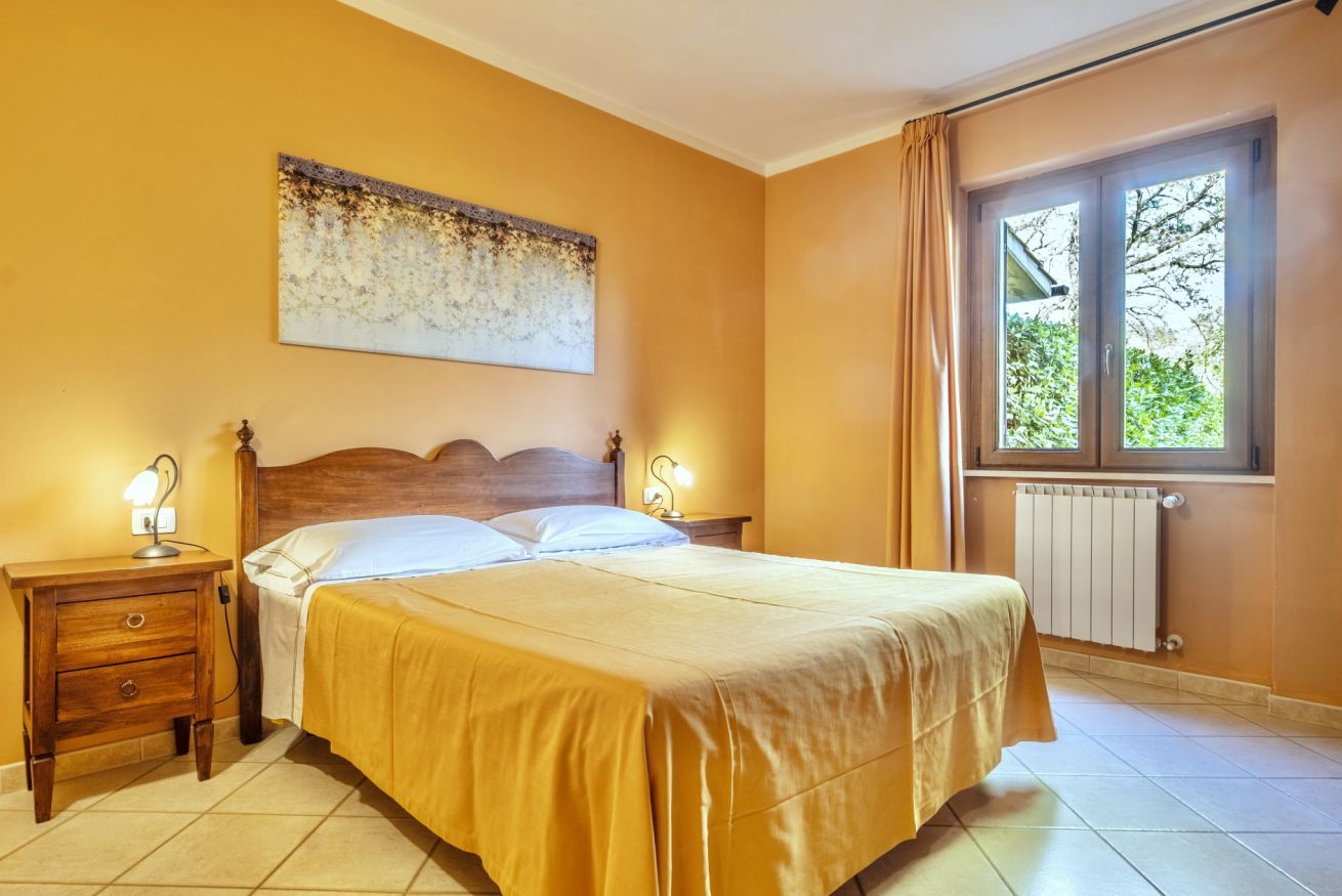 Une chambre à coucher avec un lit en bois, deux tables de chevet avec des lampes, un radiateur et une fenêtre avec des rideaux.