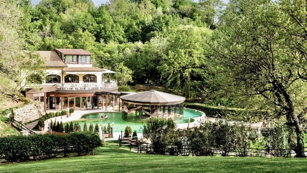 Une grande maison avec une piscine, entourée d’une végétation luxuriante et d’arbres.