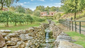 Un ruisseau aux berges en pierre, avec une cascade, entouré d’une végétation luxuriante et d’un mur de pierres.