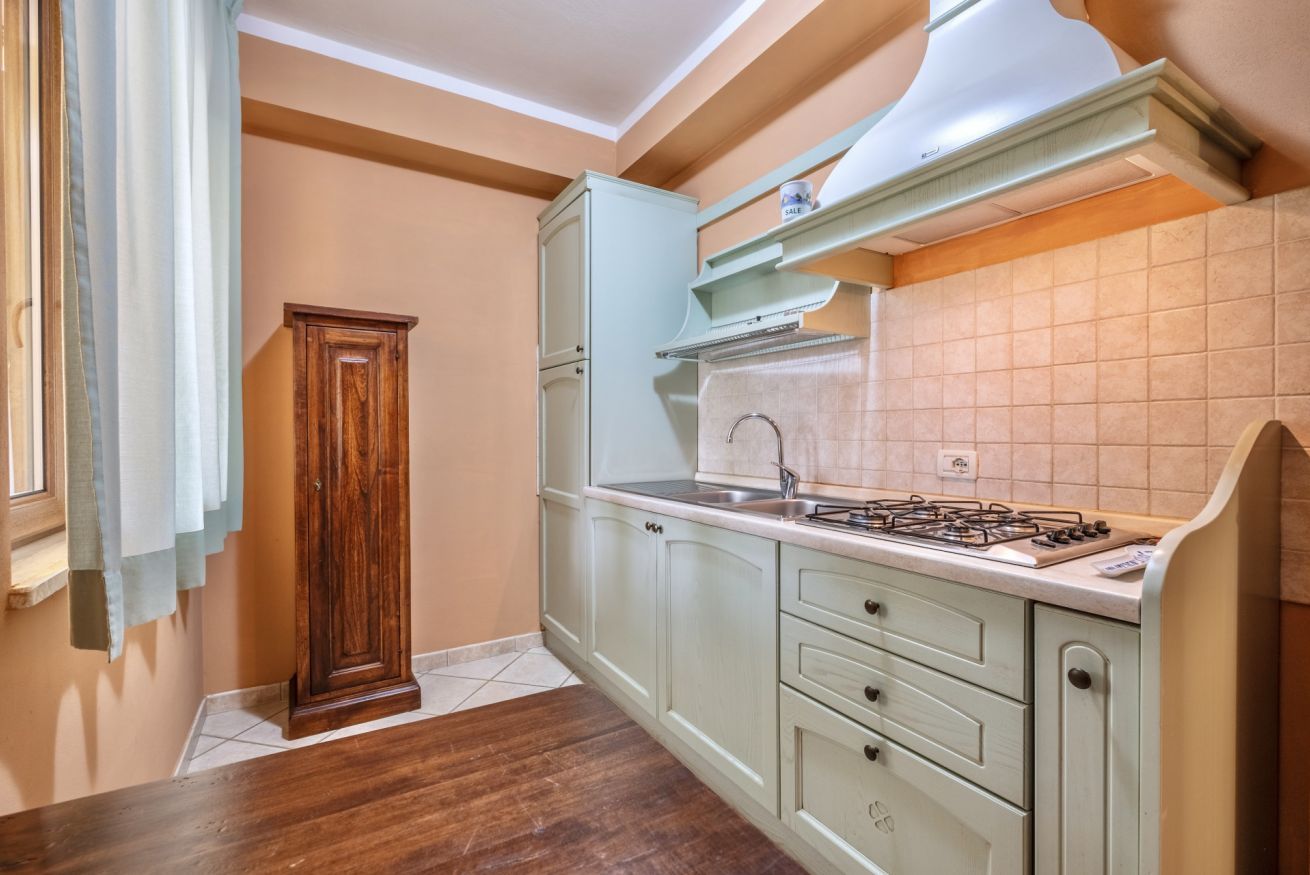 Una cocina con gabinetes verde claro, una estufa a gas y un ventanal con cortinas.