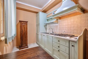 A kitchen with light green cabinets, a gas stove, and a window with curtains.