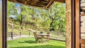Une terrasse extérieure avec une table et des chaises, entourée d’un mur de pierre et offrant une vue sur une colline boisée.