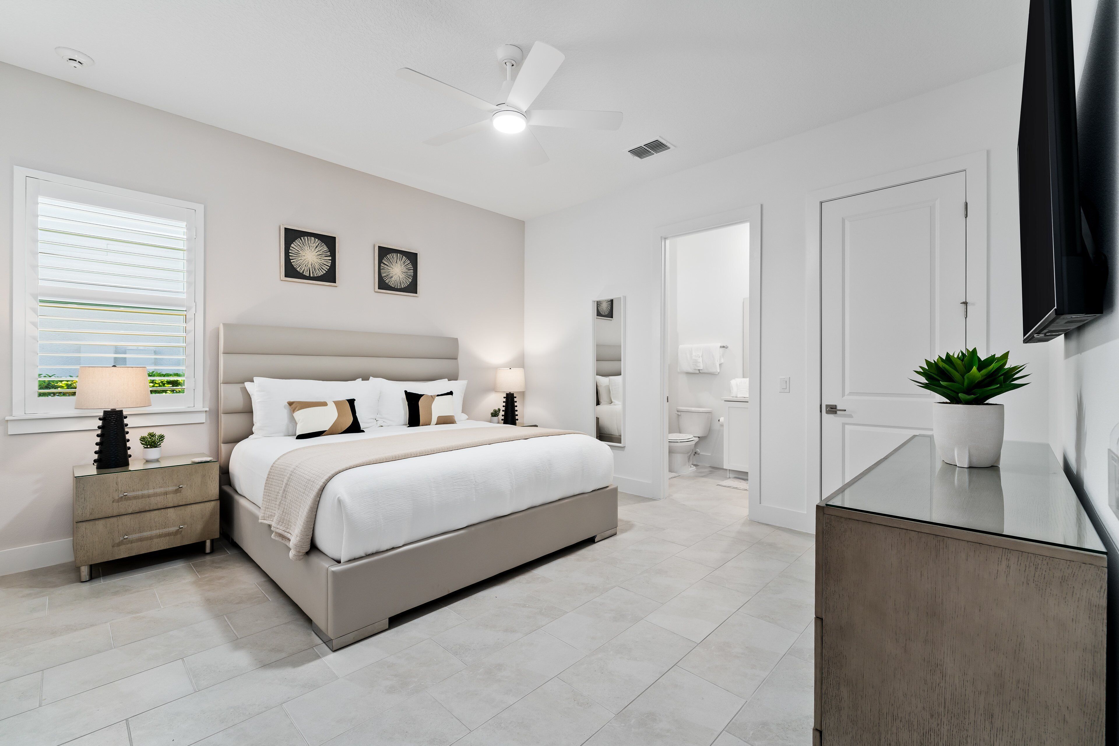 A modern bedroom with a bed, bedside tables, a ceiling fan, and a potted plant.