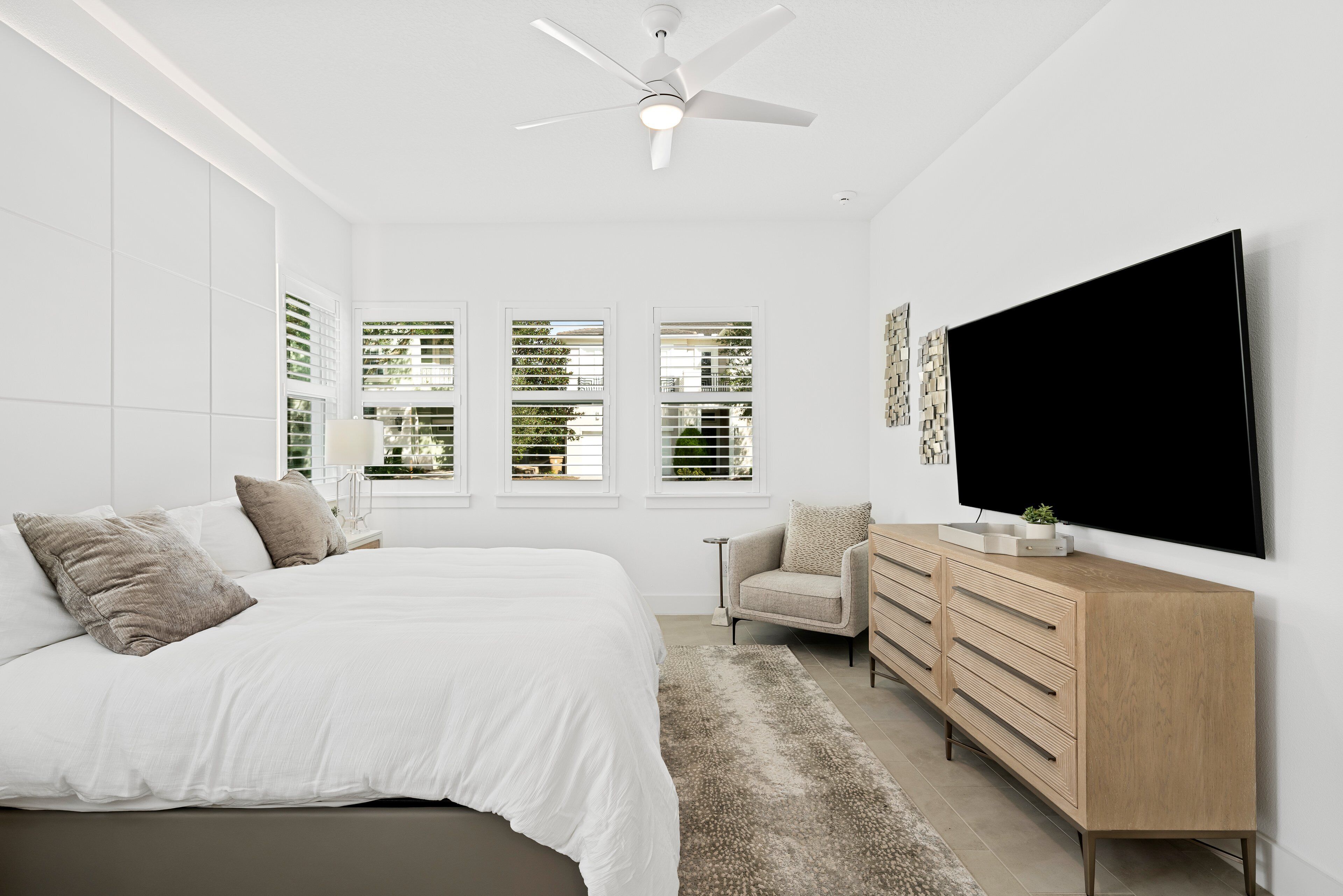 Un dormitorio moderno con una cama grande, un escritorio, una silla y un televisor montado en la pared.