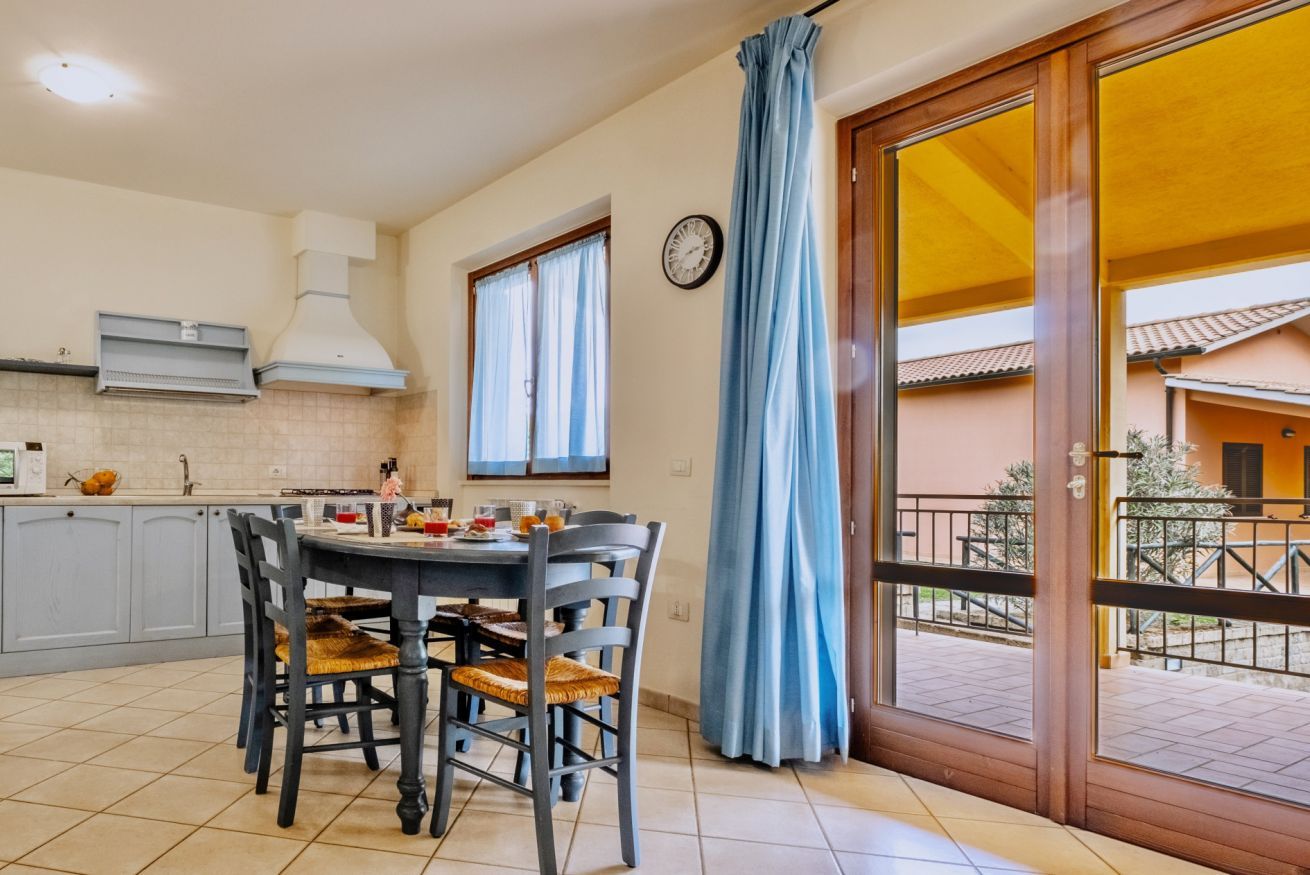 Un comedor con mesa y sillas, una cocina con armarios y estufa, y vista a un edificio a través de una ventana.